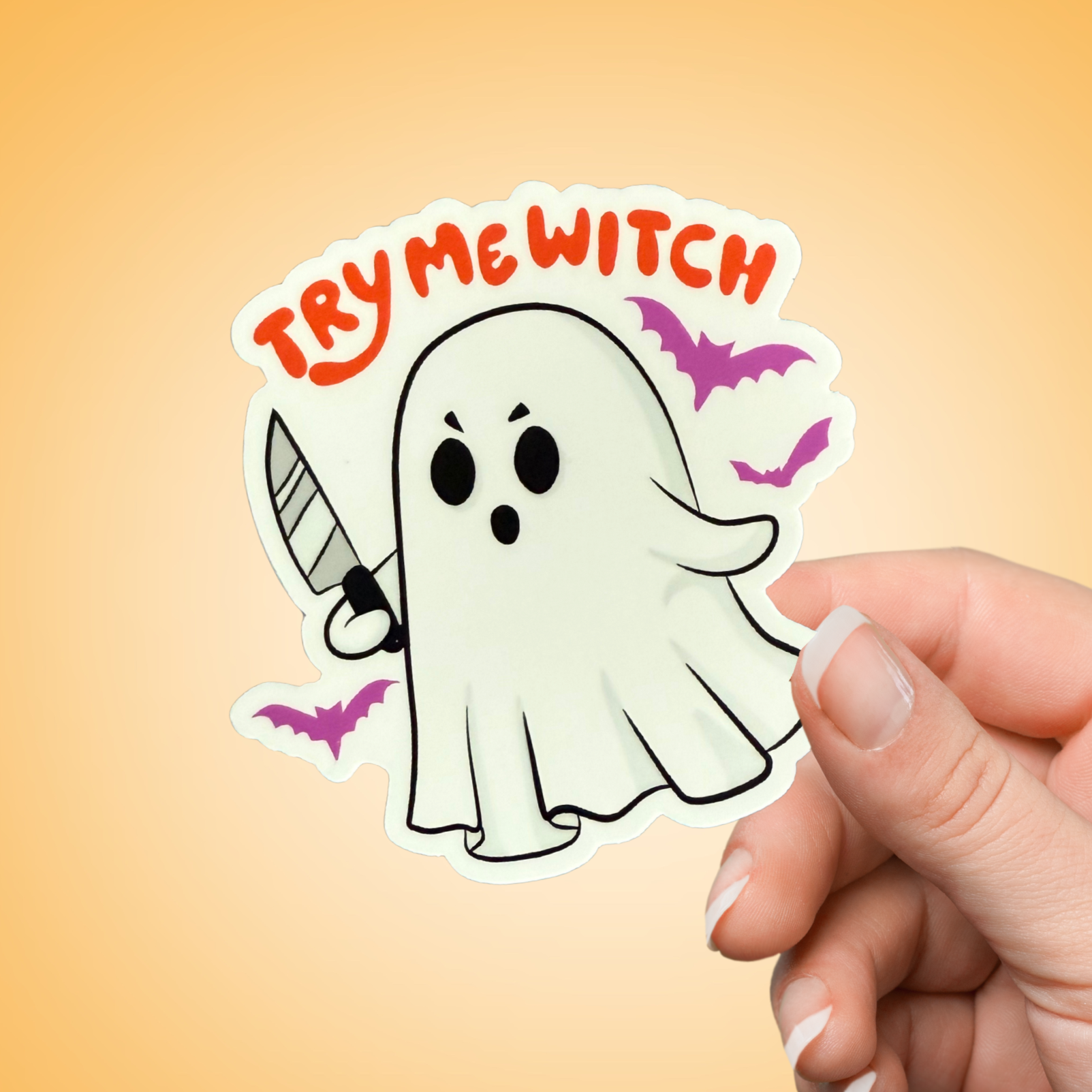Hand holding a sticker with a ghost and 'TRY ME WITCH' text on an orange background